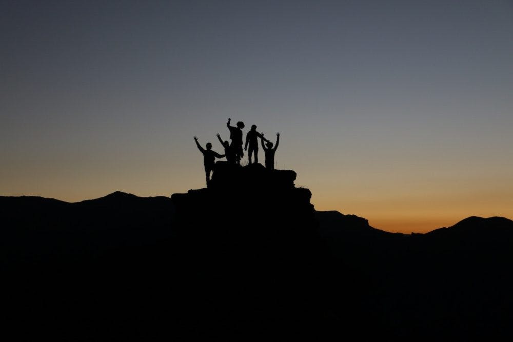 Siluetter av personer på berg i solnedgången
