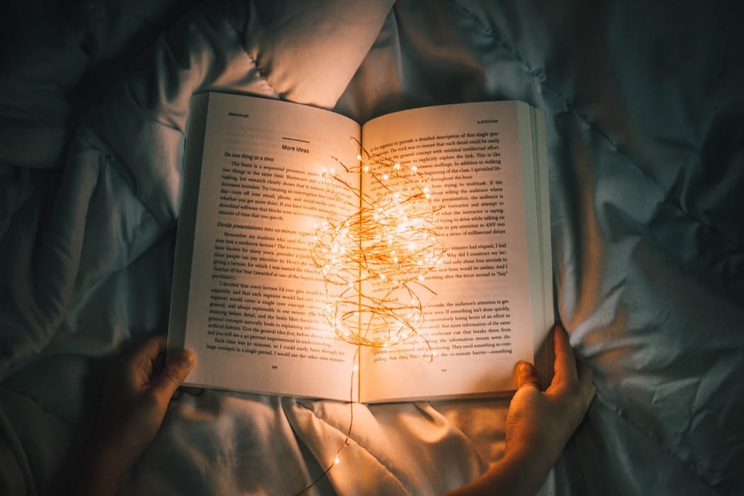 Öppen bok i säng med ljusslinga i, akademibokhandeln case