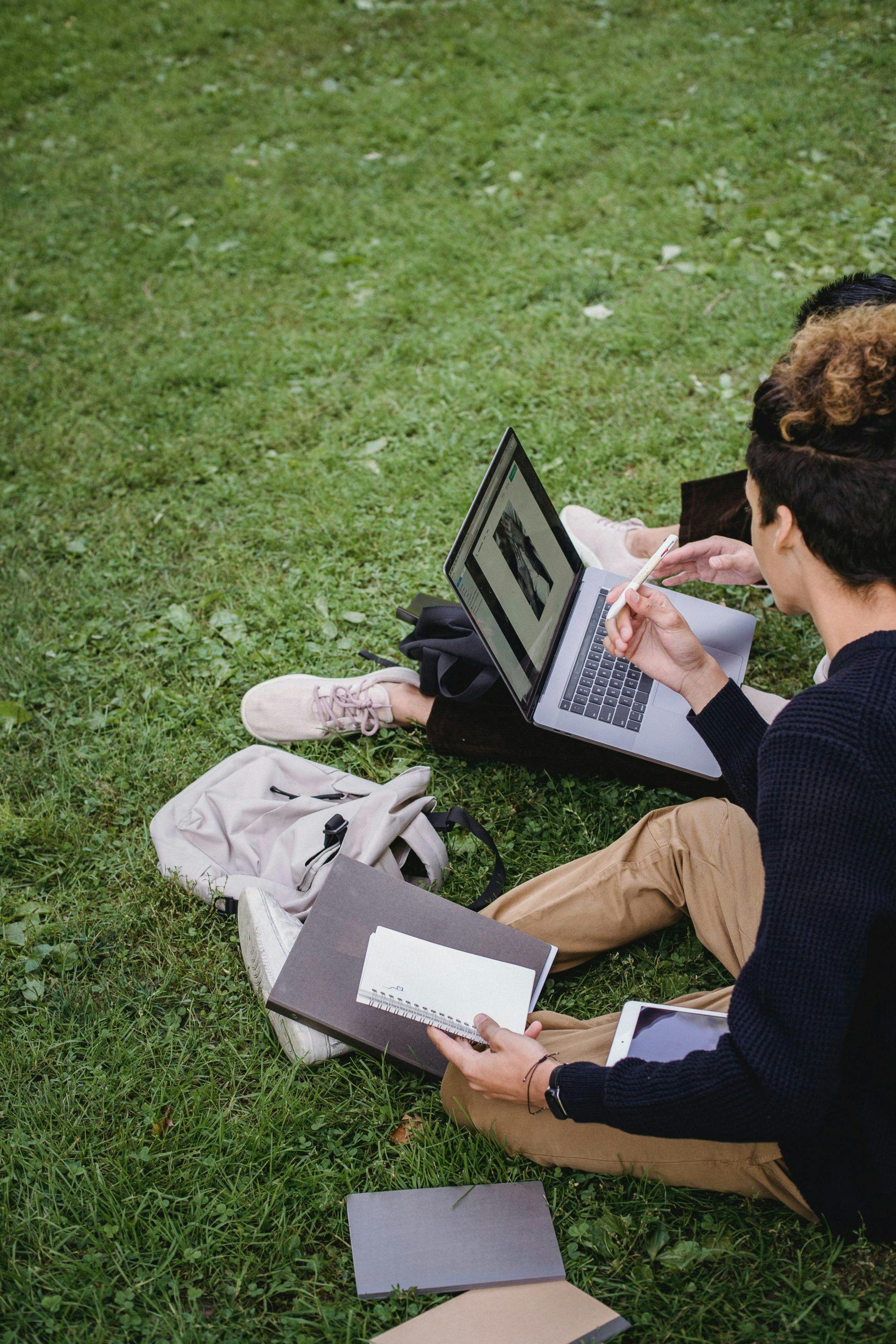 Personer som sitter i gräset med dator och anteckningsblock.
