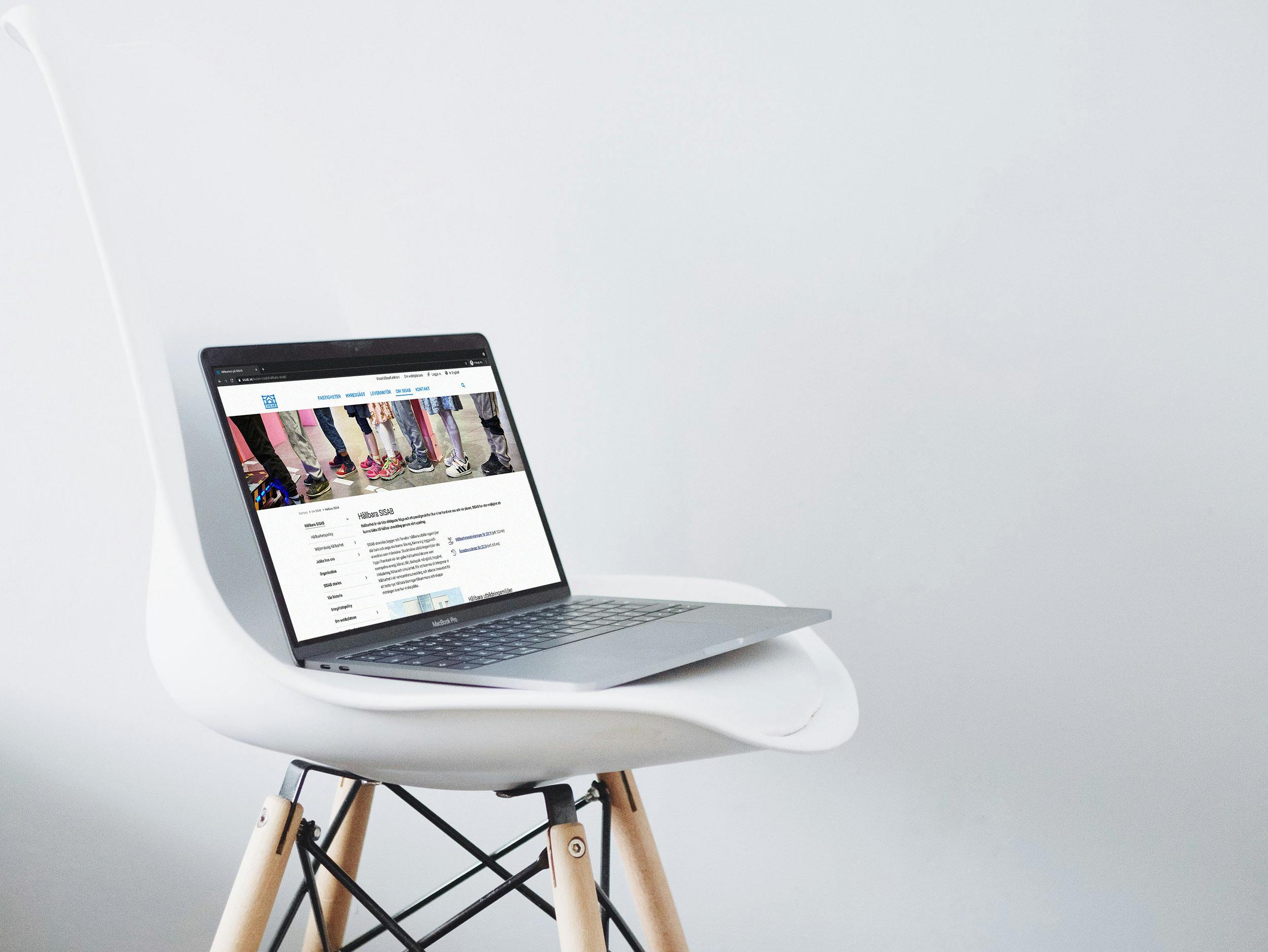 En MacBook på en vit stol med träben i en helt vit fotostudio där SISABS nya webbplats syns på skärmen