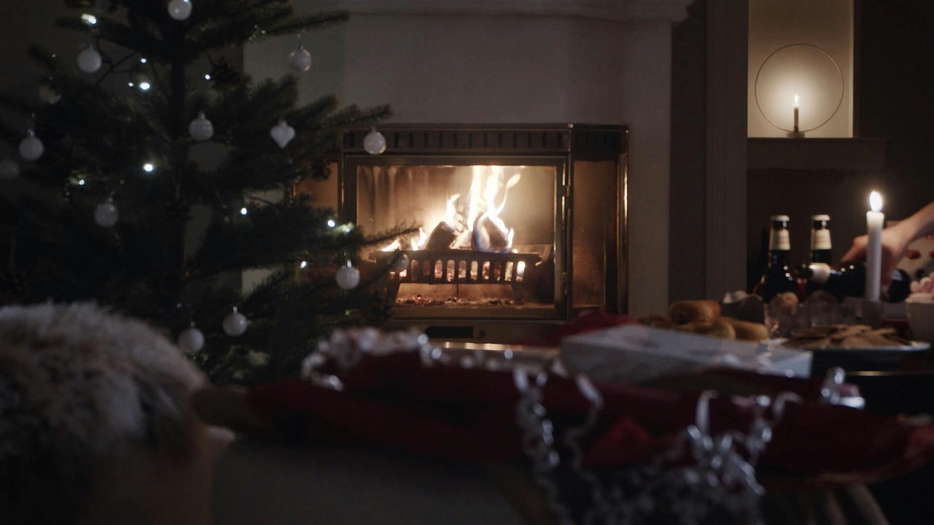 En brinnande brasa i ett julpyntat rum där det står julfika på bordet intill en julgran