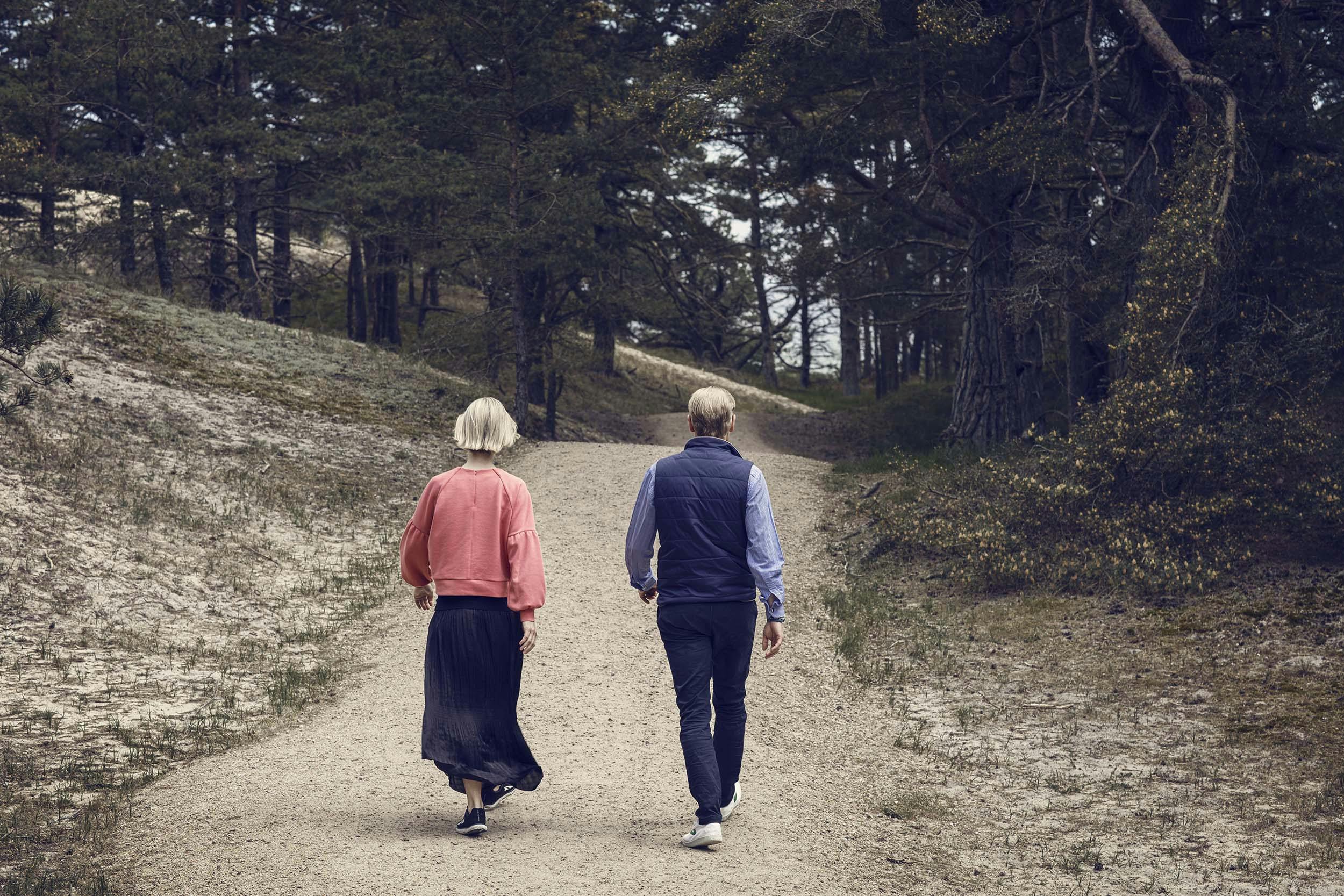 An elderly couple walking into a forest on a path