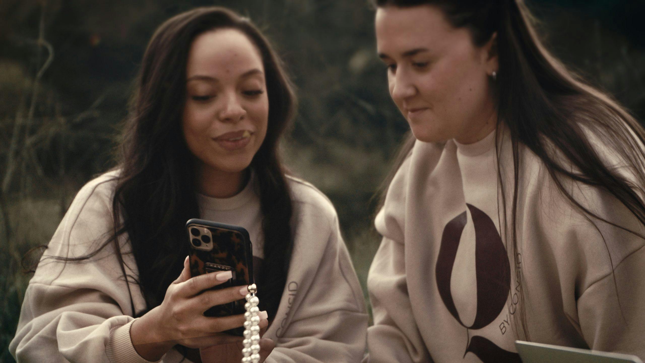 Två kvinnor som interagerar genom att den ena visar den andra något på telefonen.