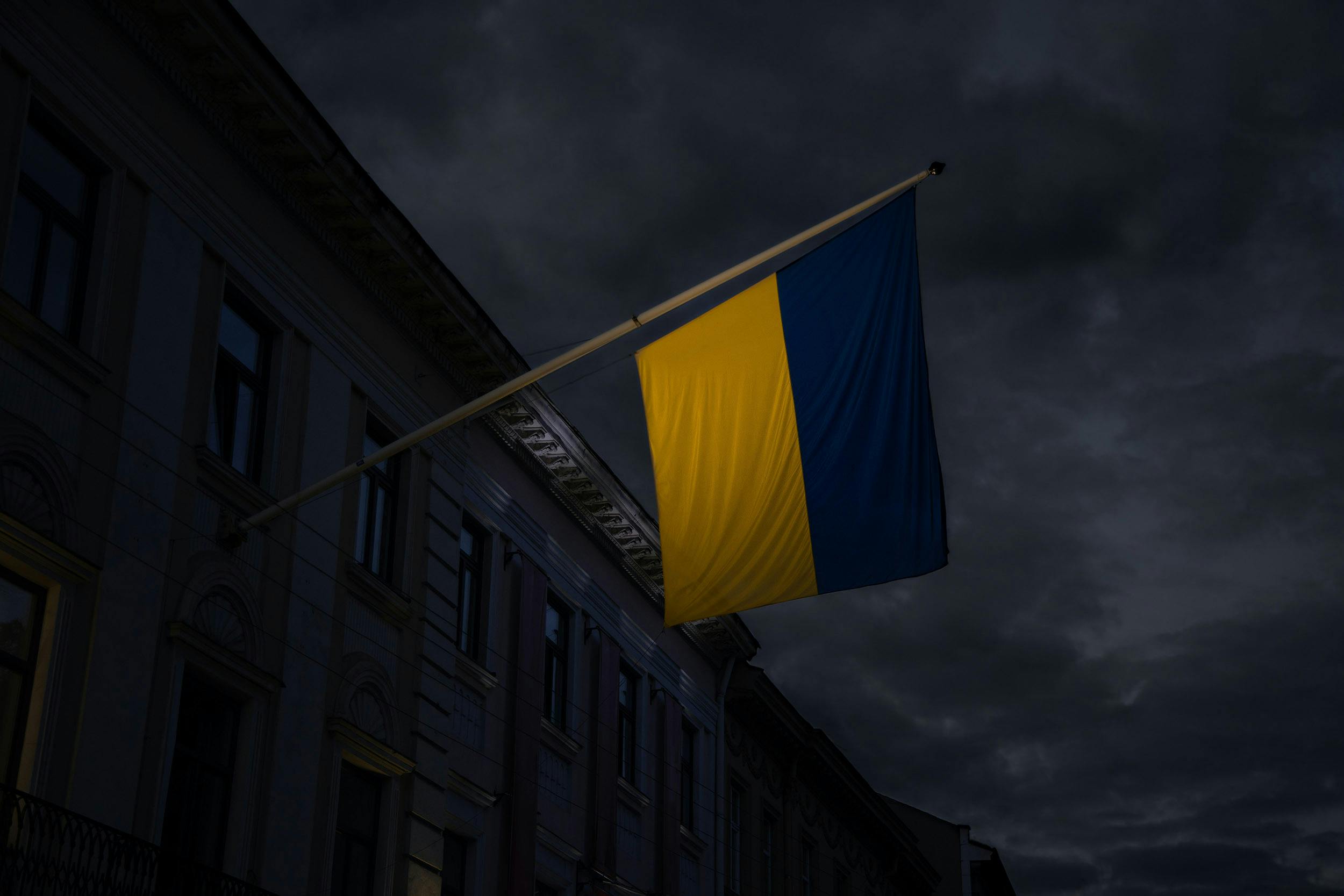 En ukrainsk flagga hängandes från en flaggstång monterad på vägg i mörk omgivning