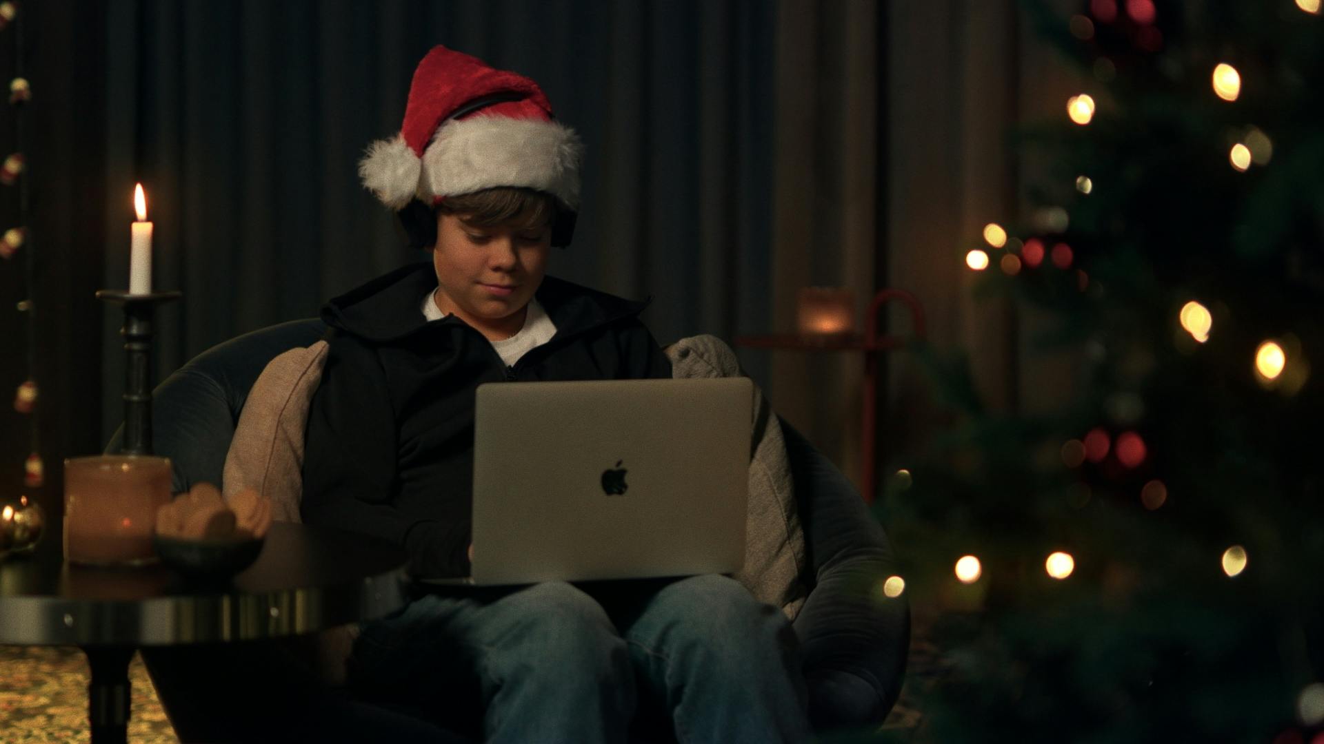 Barn som sitter med datorn i knät intill en julgran med tomteluva på ett Consid-kontor