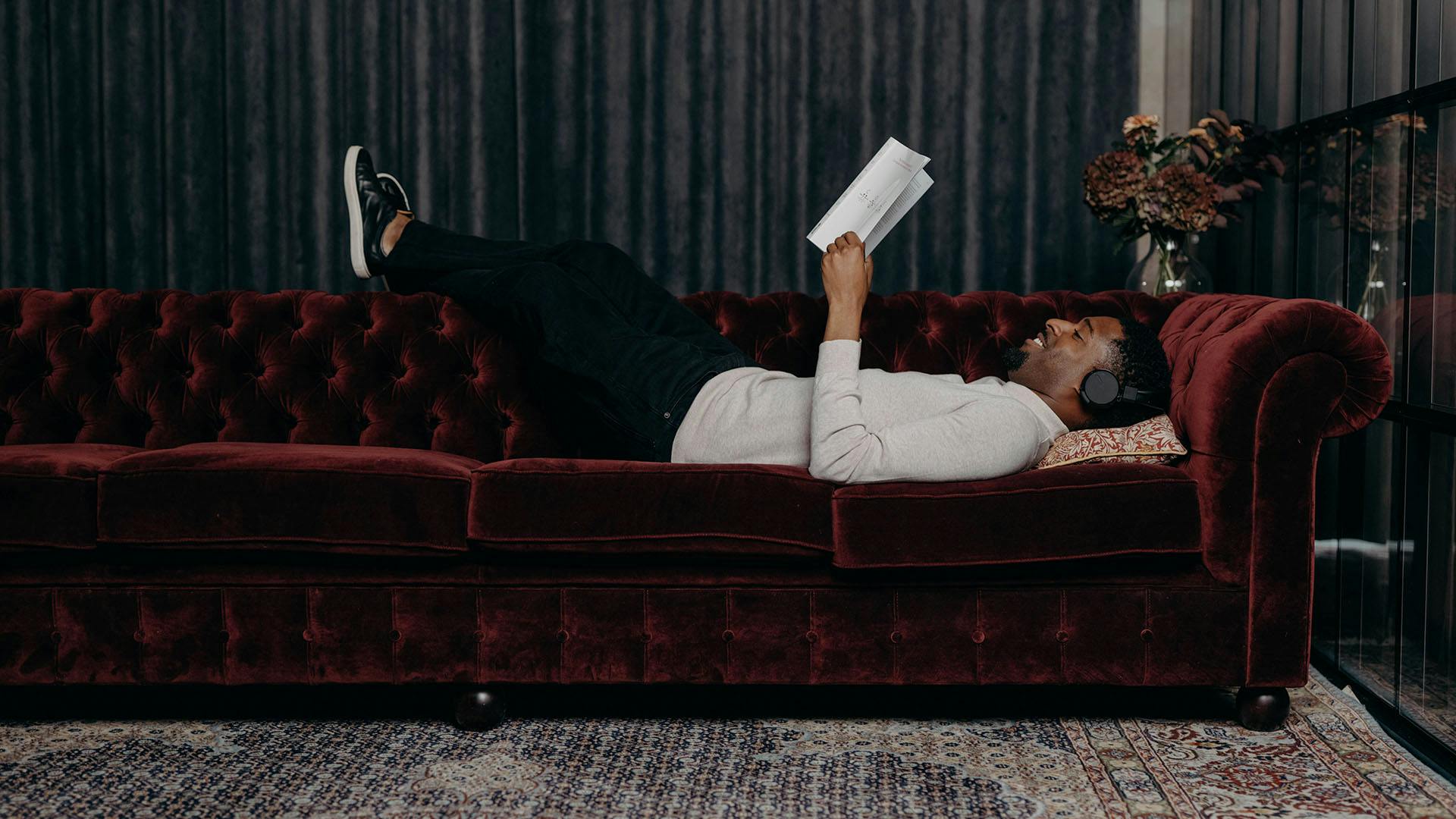 Man laying down on a sofa reading a book